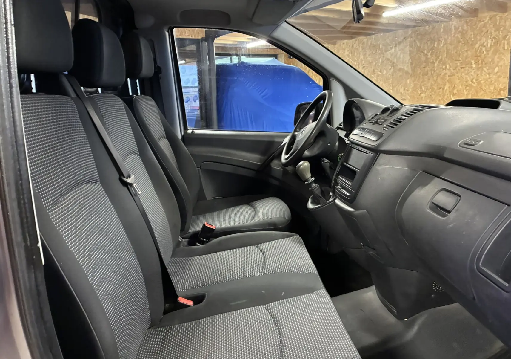 Vue intérieure côté conducteur du Mercedes Vito gris 2012, montrant les sièges tissu noirs et la console avec boîte manuelle.