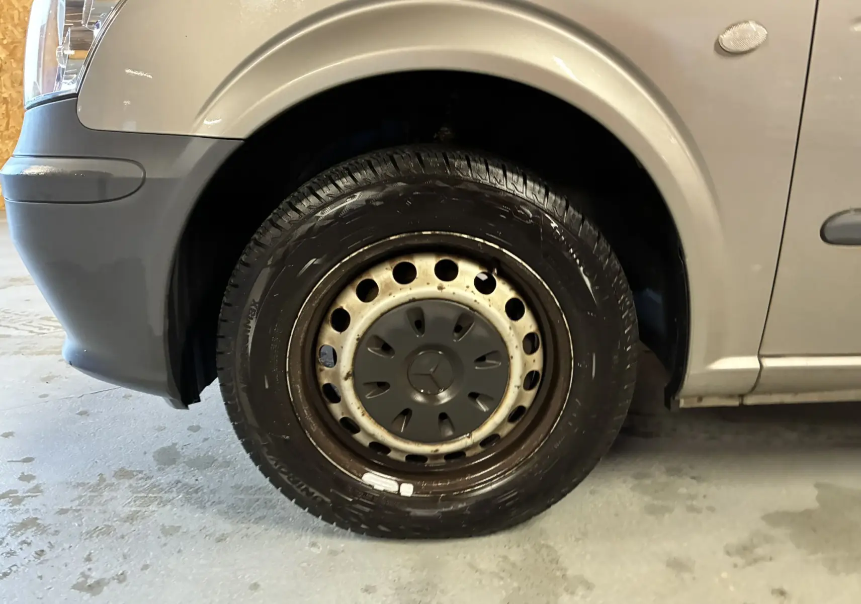 Gros plan sur la roue avant gauche grise d’un Mercedes Vito 2.8 113 CDI Fourgon Long de 2012 avec jante acier et enjoliveur noir.