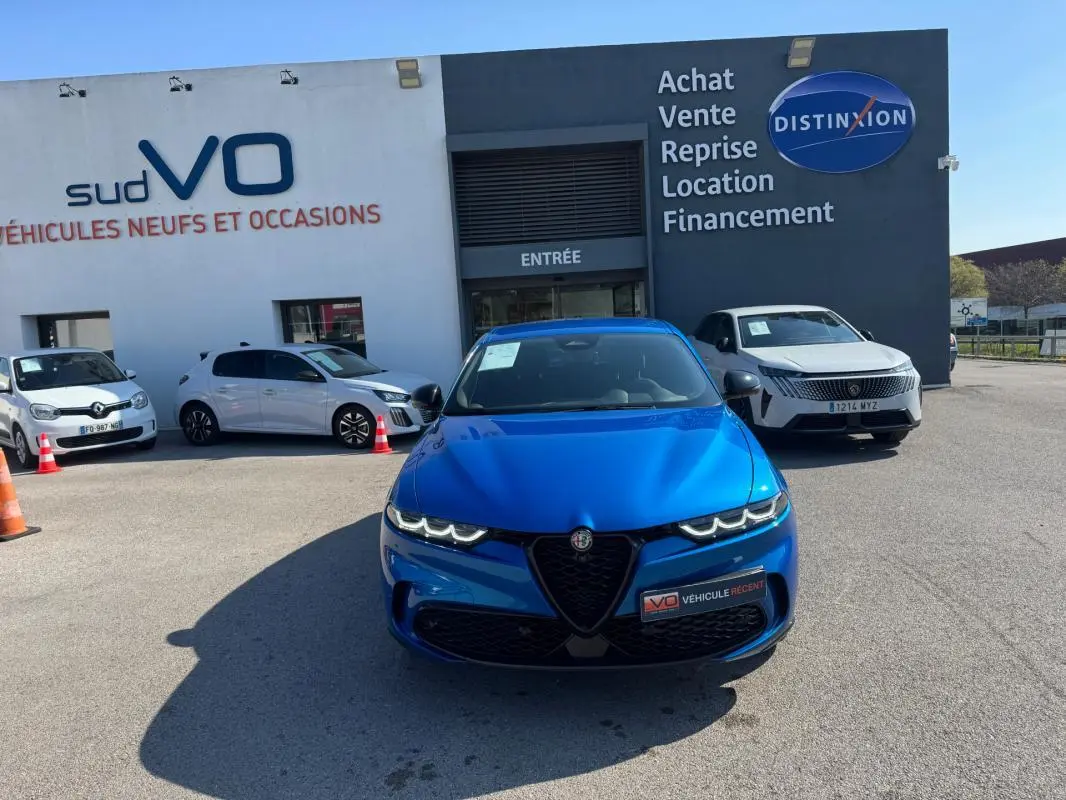 Vue avant d'un Alfa Romeo Tonale bleu foncé 2025, avec calandre caractéristique et phares LED allumés, devant un concessionnaire.