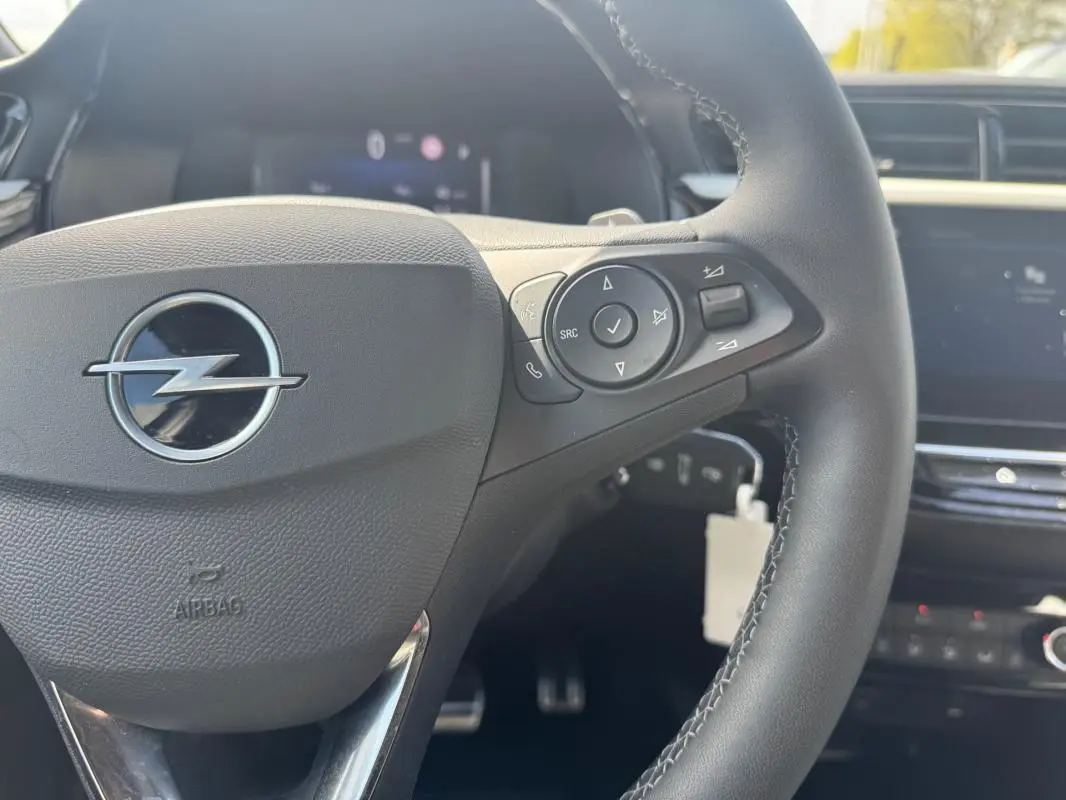 Gros plan sur le volant noir de l’Opel Corsa 2025 avec commandes intégrées et logo Opel central argenté.