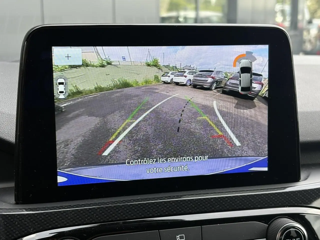 Écran tactile intérieur montrant la caméra de recul du Ford Kuga bleu azur, avec lignes de guidage et vue arrière.
