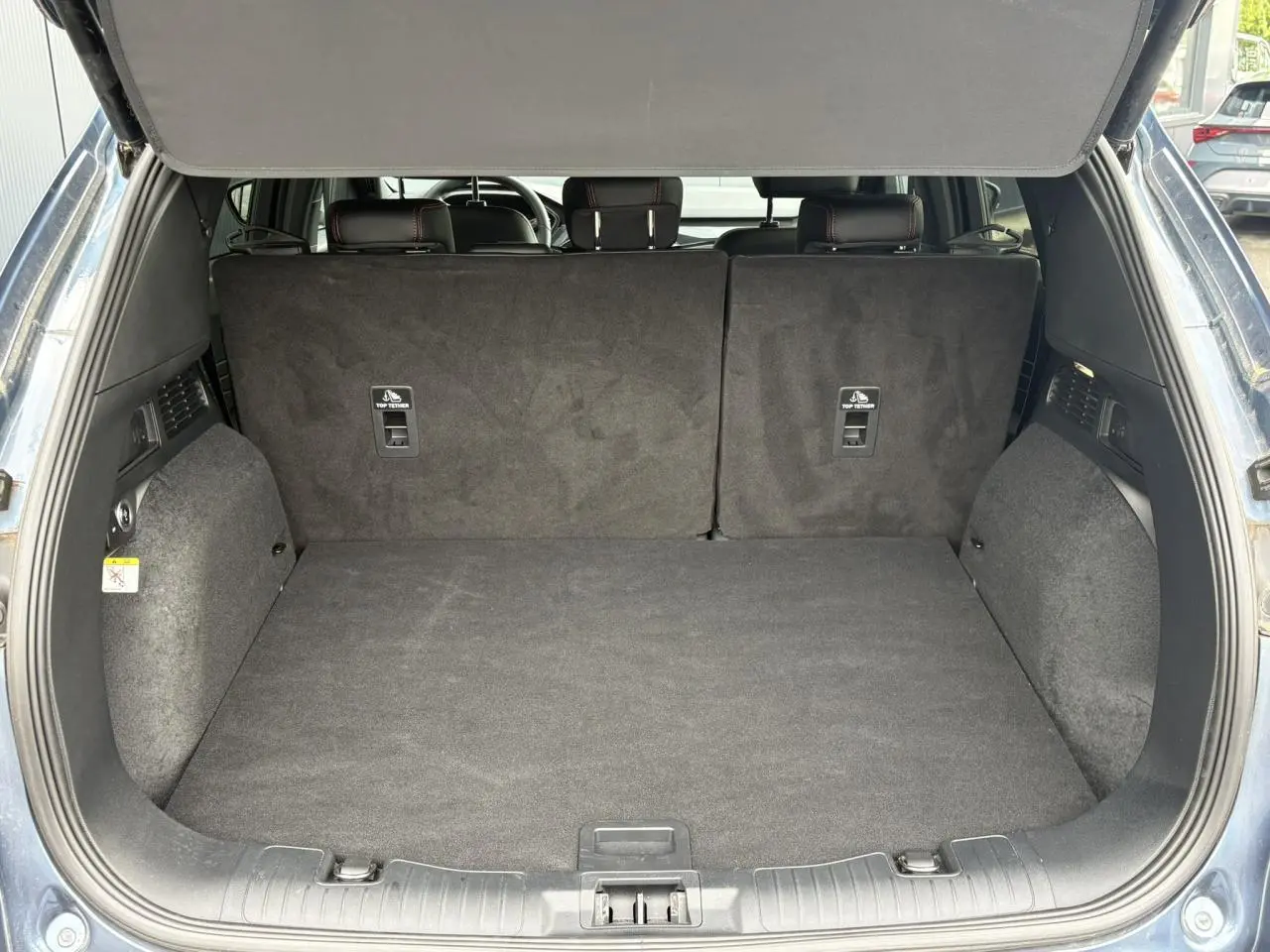 Coffre ouvert vu de l'arrière d'un Ford Kuga bleu azur, banquette arrière noire avec surpiqûres rouges visible.