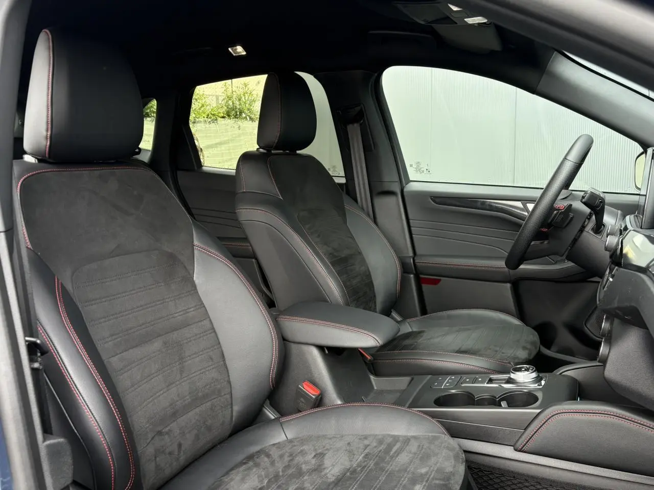 Vue intérieure côté conducteur du Ford Kuga ST-Line X 2023, sièges noirs avec surpiqûres rouges et volant sport à méplat.
