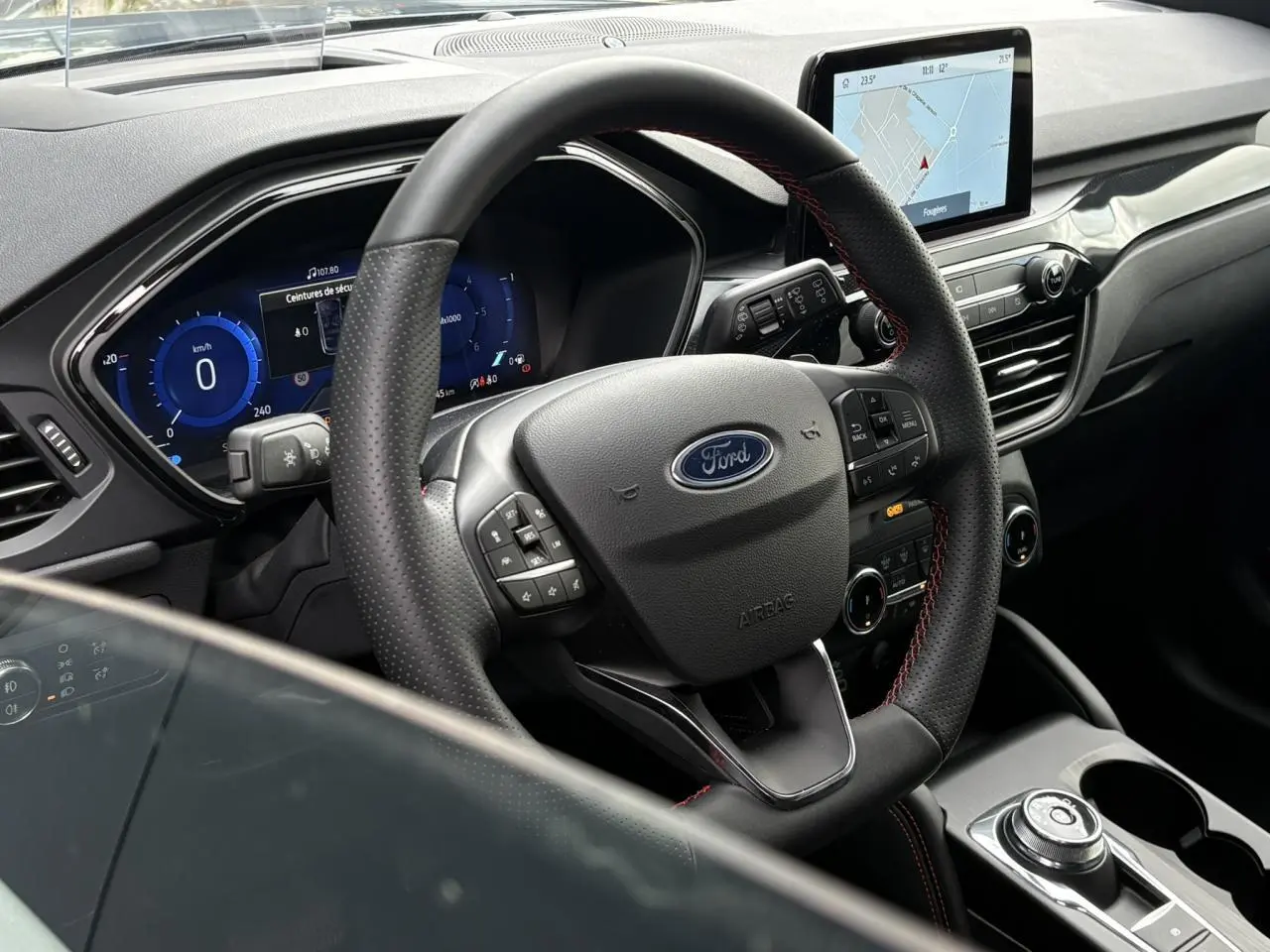 Vue intérieure centrée sur le volant ST-Line noir avec surpiqûres rouges et écran tactile du Ford Kuga 2023.