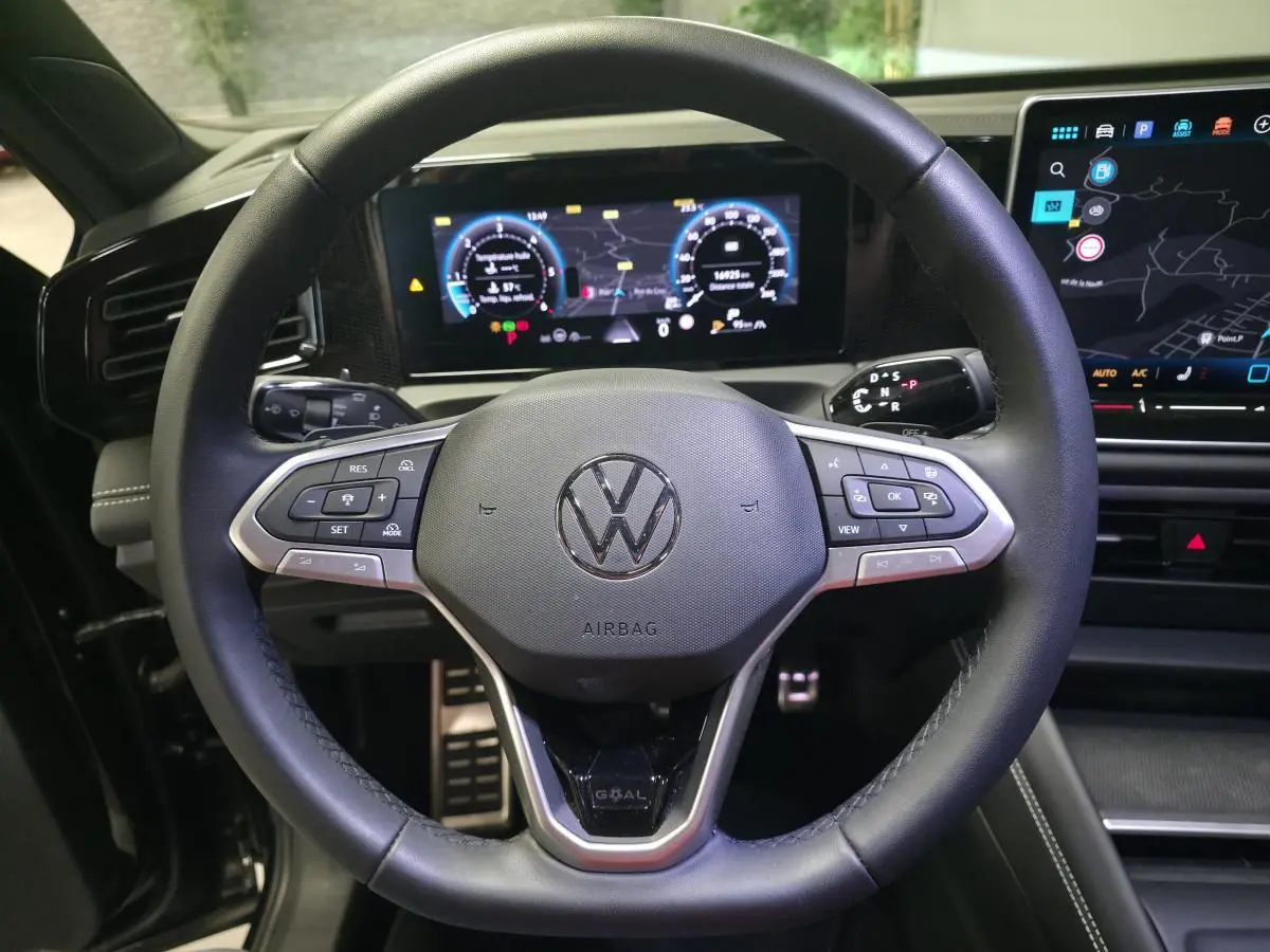 Vue intérieure centrée sur le volant cuir noir du Volkswagen Tiguan 2025 avec tableau de bord numérique et écran tactile.