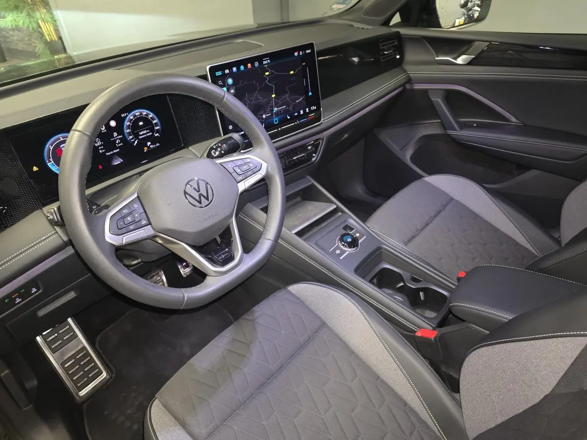 Vue intérieure côté conducteur du Volkswagen Tiguan 2025 noir, avec tableau de bord numérique et sièges tissu gris.