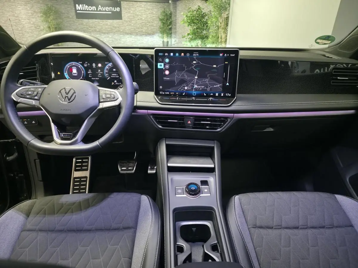 Vue intérieure avant du Volkswagen Tiguan noir 2025, tableau de bord numérique et écran tactile central avec navigation.