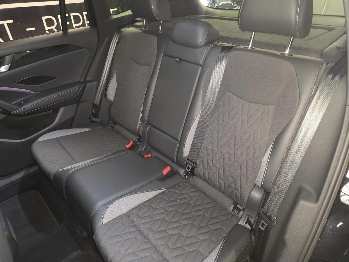 Vue intérieure de la banquette arrière noire et grise du Volkswagen Tiguan 2025 avec ceintures et appuie-têtes visibles.