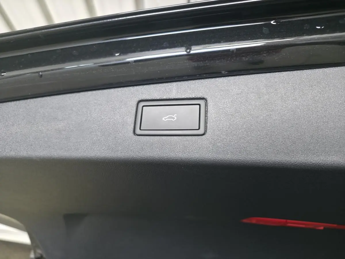 Bouton d'ouverture électrique du hayon sur le bord intérieur du coffre d'un Volkswagen Tiguan noir.