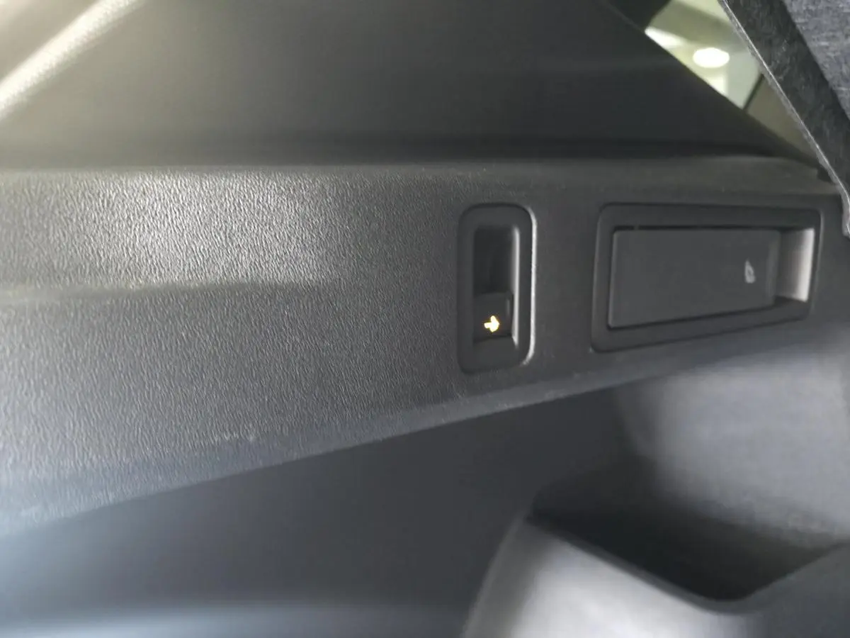 Détail du bouton d'ouverture électrique du hayon dans le coffre du Volkswagen Tiguan noir 2025.