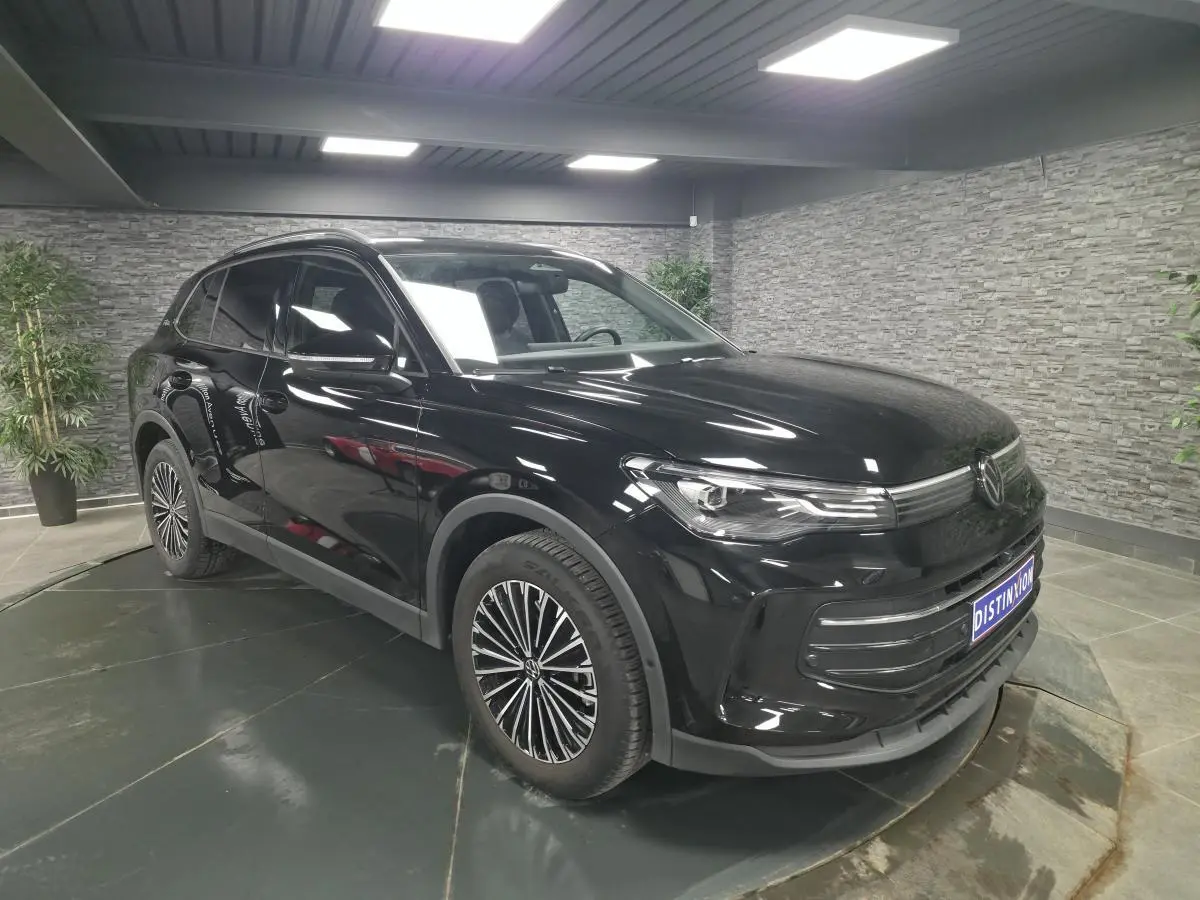 Volkswagen Tiguan noir en 3/4 avant droit, jantes alliage distinctives, stationné en intérieur moderne.