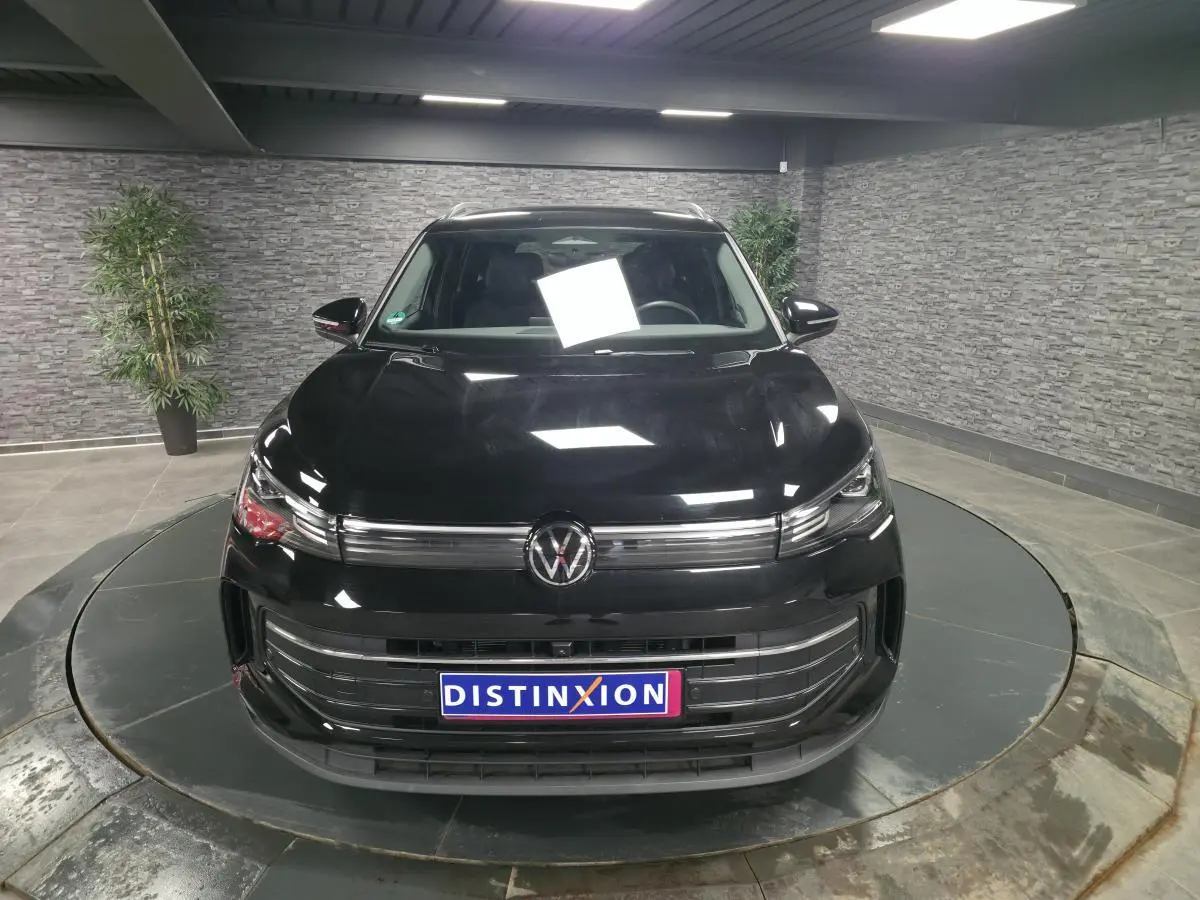 Vue avant d'un Volkswagen Tiguan noir 2025 avec calandre chromée et plaque Distinxion en intérieur showroom.