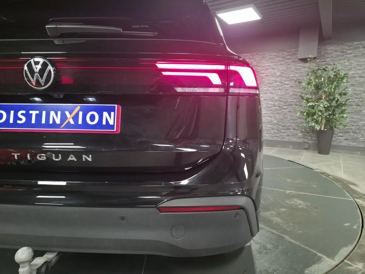 Vue arrière droite d’un Volkswagen Tiguan noir avec feux LED allumés et crochet d’attelage visible en showroom.