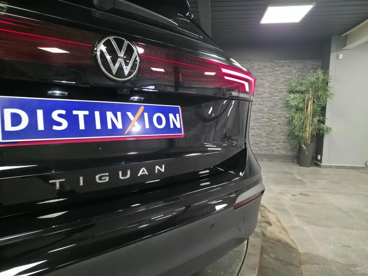 Vue arrière rapprochée du Volkswagen Tiguan noir avec feux LED allumés et logo distinctif sur fond intérieur showroom.