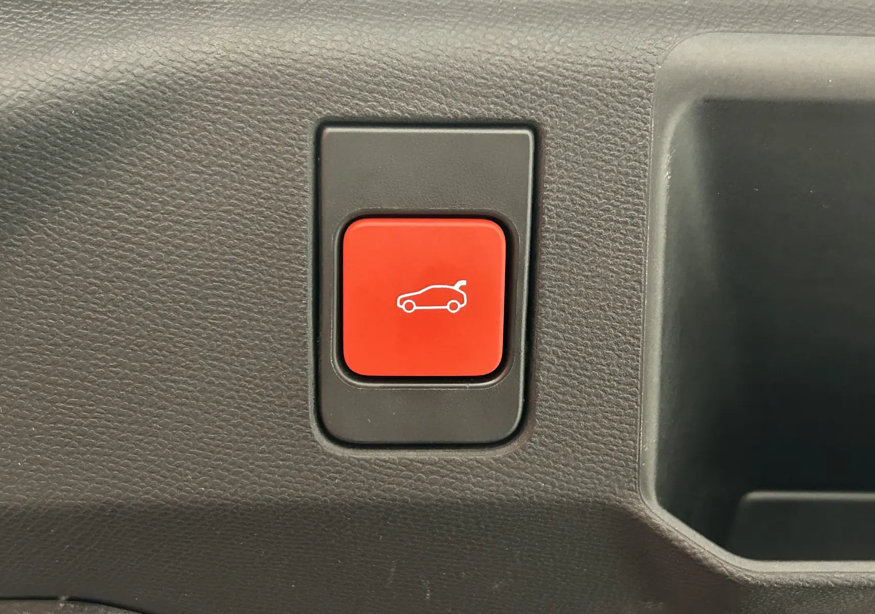 Bouton rouge d'ouverture électrique du hayon sur tableau de bord noir d'un Peugeot 5008 blanc hybride 2025.