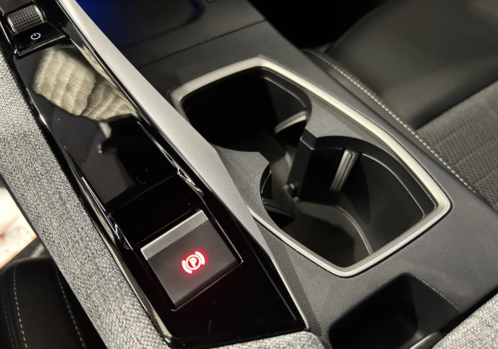 Gros plan sur la console centrale noire et grise avec porte-gobelets et bouton frein à main électrique allumé du Peugeot 5008 blanc.