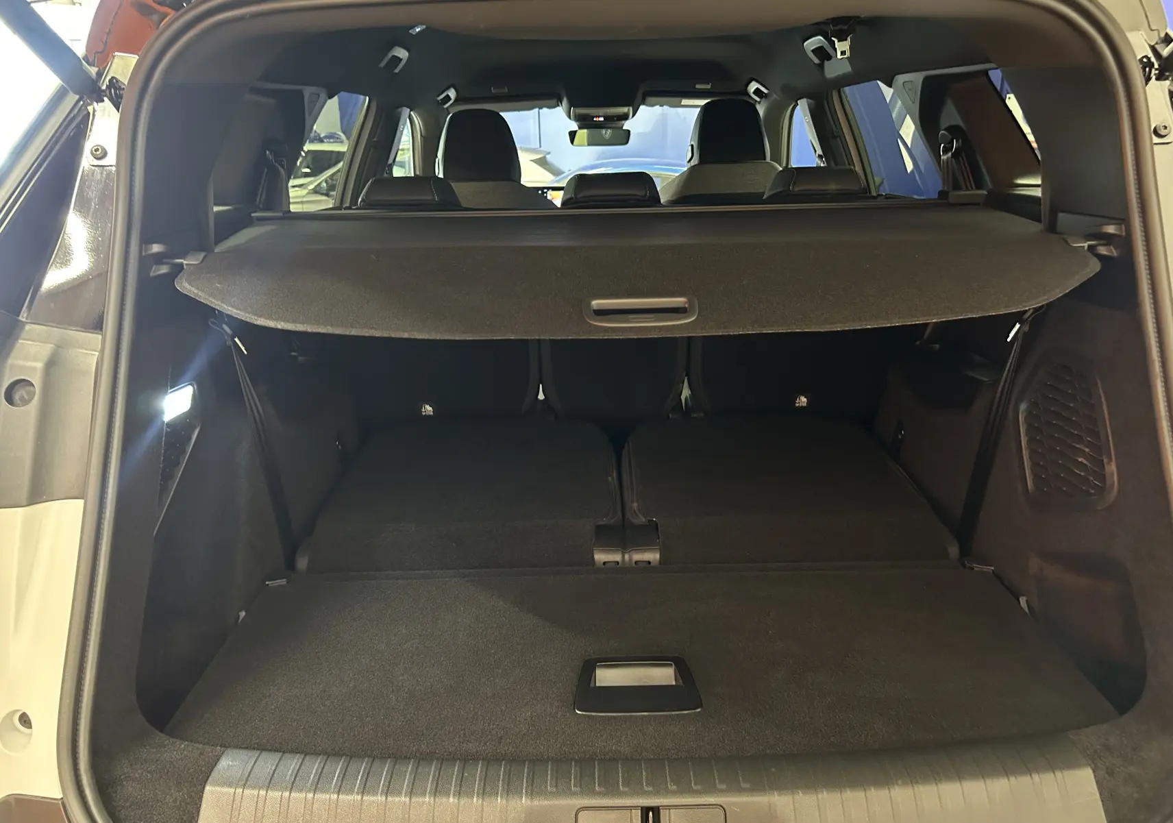 Vue arrière du coffre ouvert du Peugeot 5008 blanc avec banquette arrière rabattue et cache-bagages en place.