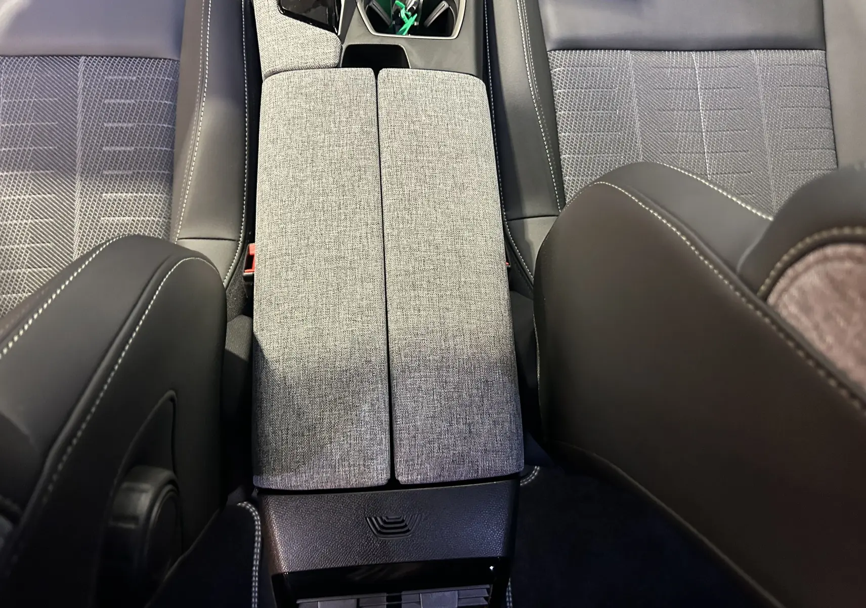 Vue plongeante sur la console centrale grise et les sièges en tissu et cuir noir de la Peugeot 5008 Hybrid 2025.