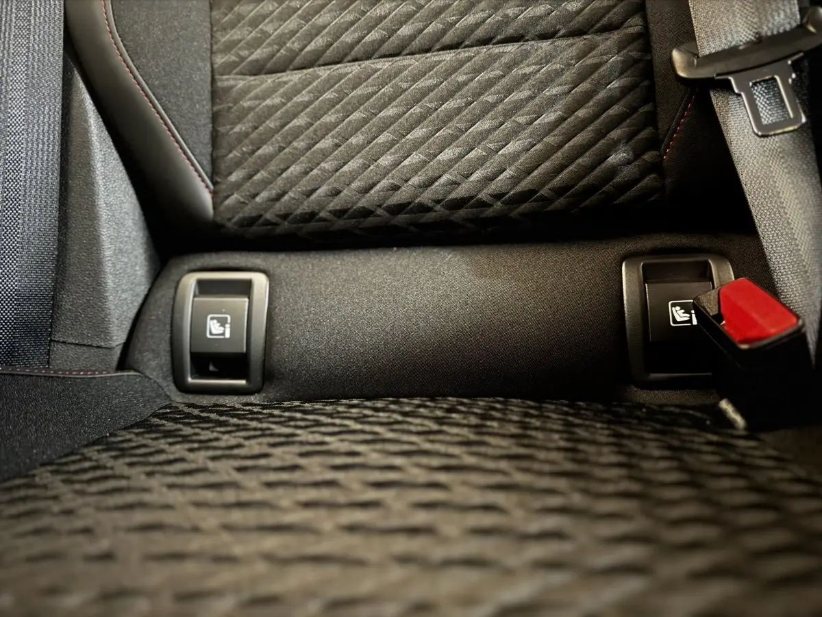 Gros plan sur les fixations Isofix arrière et la ceinture de sécurité rouge dans l’habitacle noir de la Renault Clio gris clair.