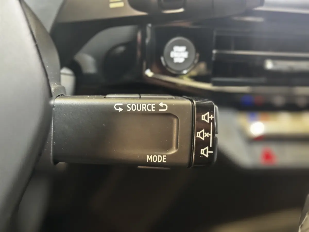 Gros plan sur la commande au volant de la Renault Clio 2026, bouton source et mode, intérieur noir flouté en arrière-plan.