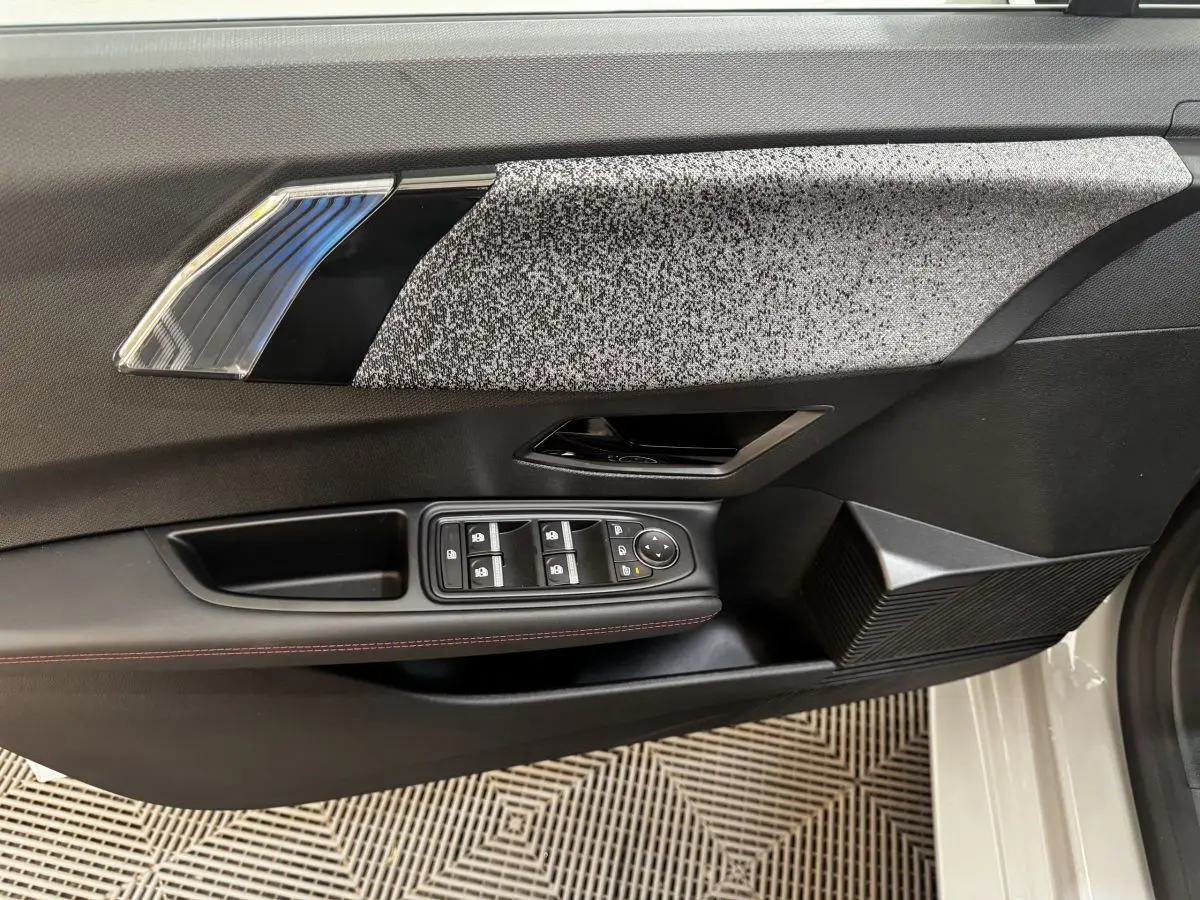 Détail de la porte avant gauche de la Renault Clio gris clair 2026 avec commandes électriques et insert décoratif texturé.