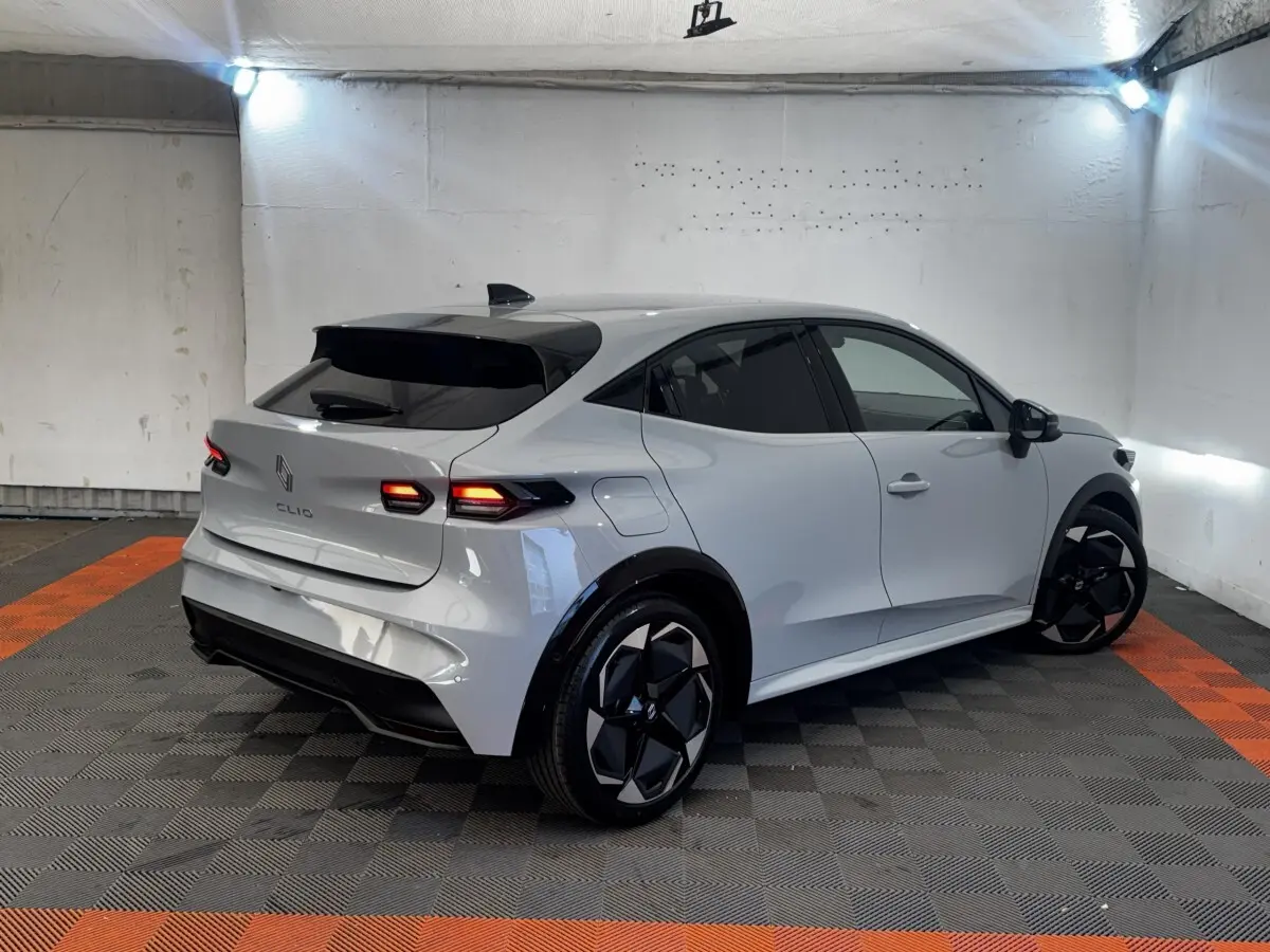 Vue 3/4 arrière droite d'une Renault Clio gris clair 2026 avec feux LED et jantes noires au design moderne.