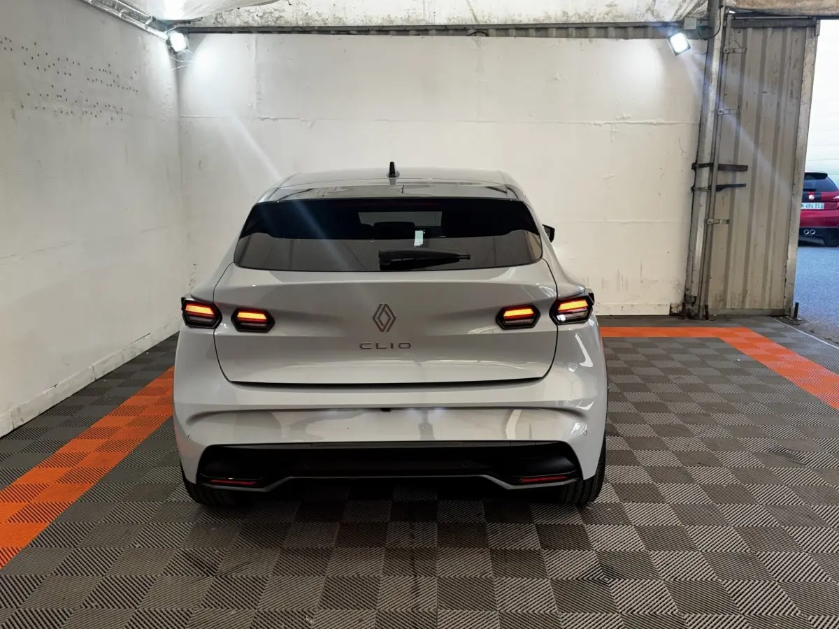 Vue arrière d'une Renault Clio gris clair 2026 avec feux LED allumés, stationnée sur un sol à damiers gris et orange.