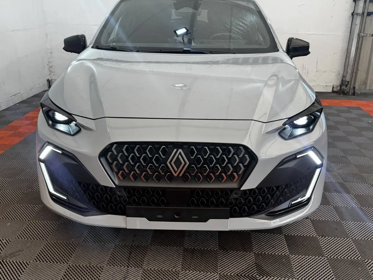 Vue frontale d'une Renault Clio gris clair 2026 avec feux LED allumés et calandre hexagonale distinctive.