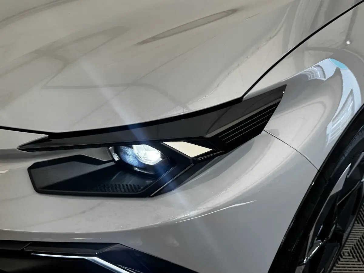 Gros plan sur le phare avant droit allumé d'une Renault Clio 2026 gris clair avec carrosserie lisse et jante noire.