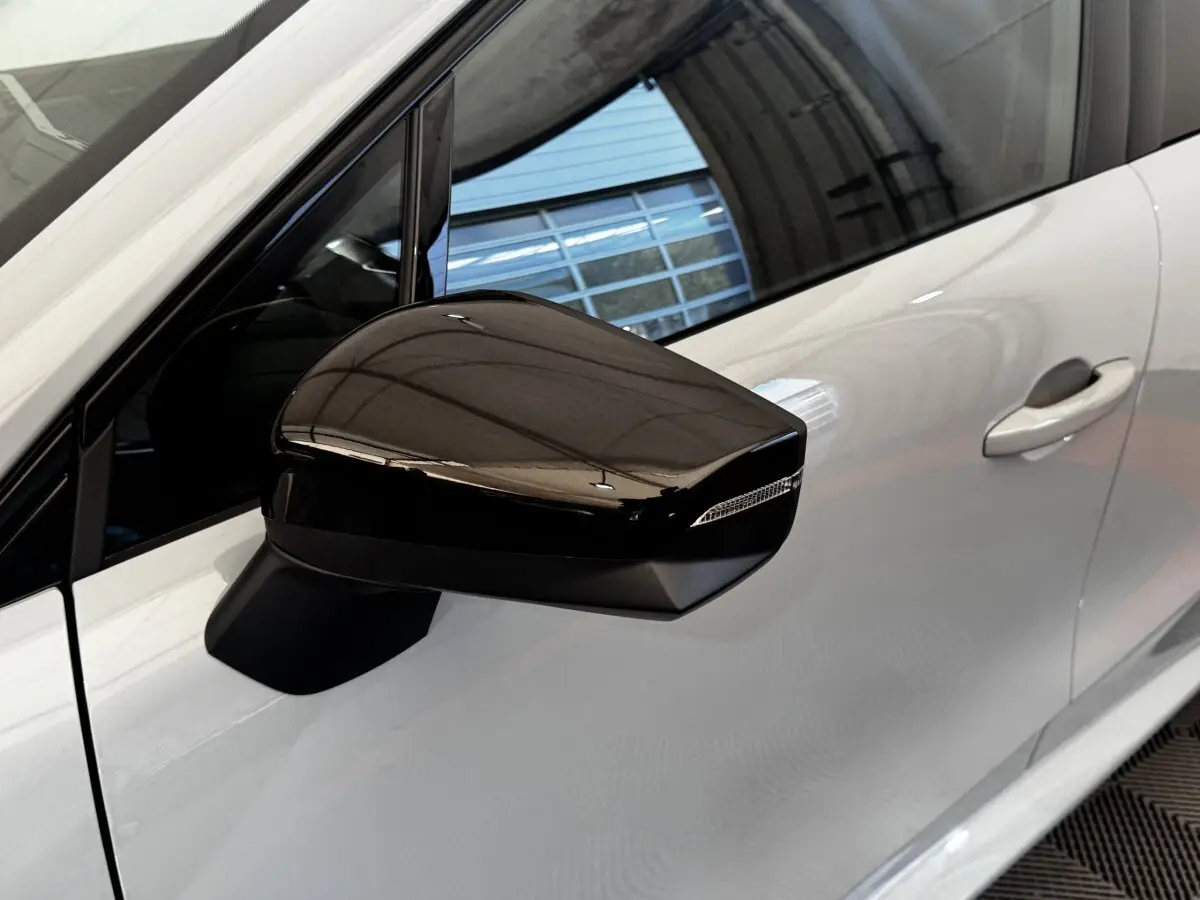 Rétroviseur droit noir brillant sur Renault Clio gris clair, vue rapprochée du côté avant droit.