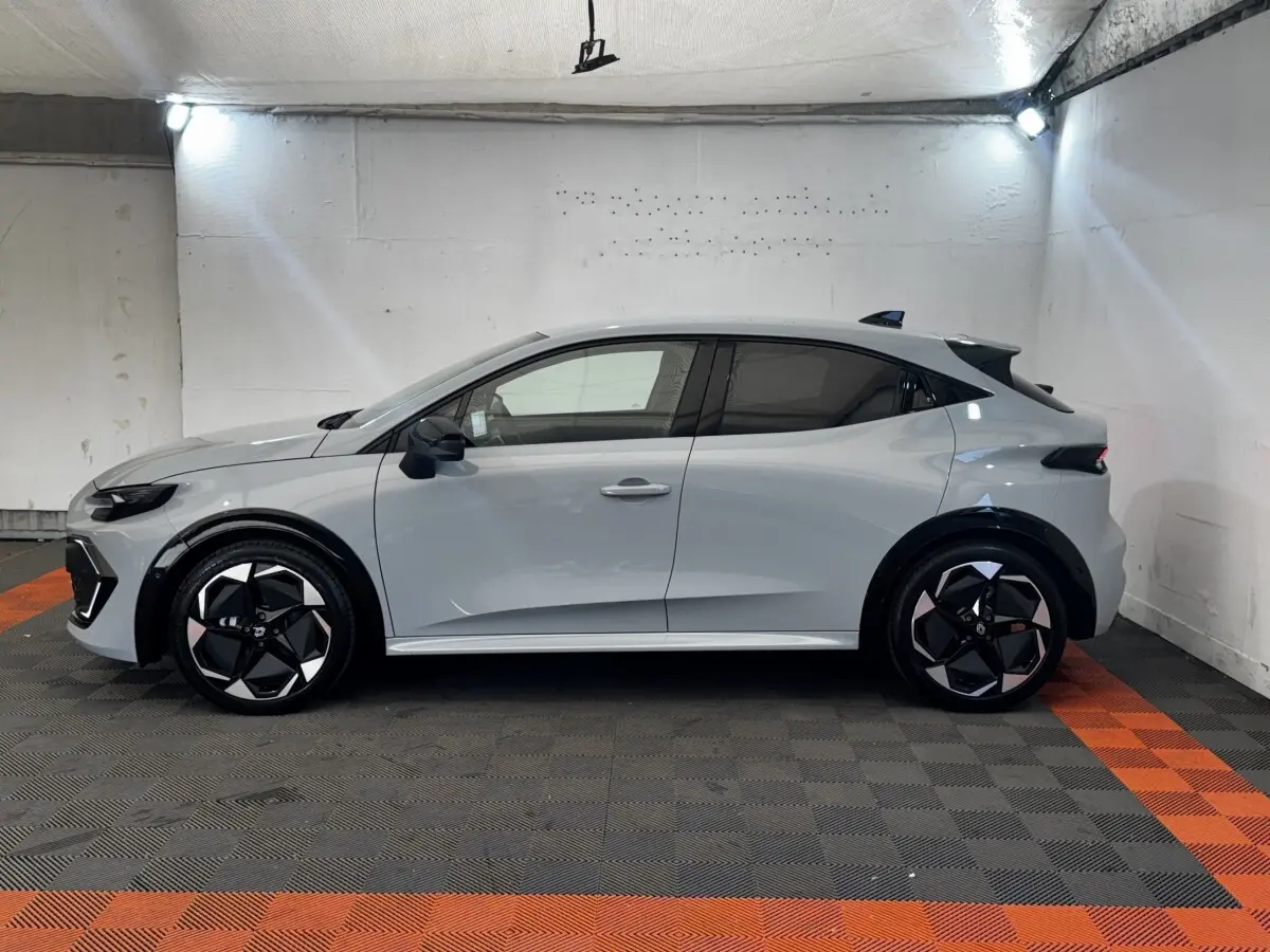 Profil droit d'une Renault Clio Techno gris clair, avec jantes noires et détails modernes en intérieur de garage.