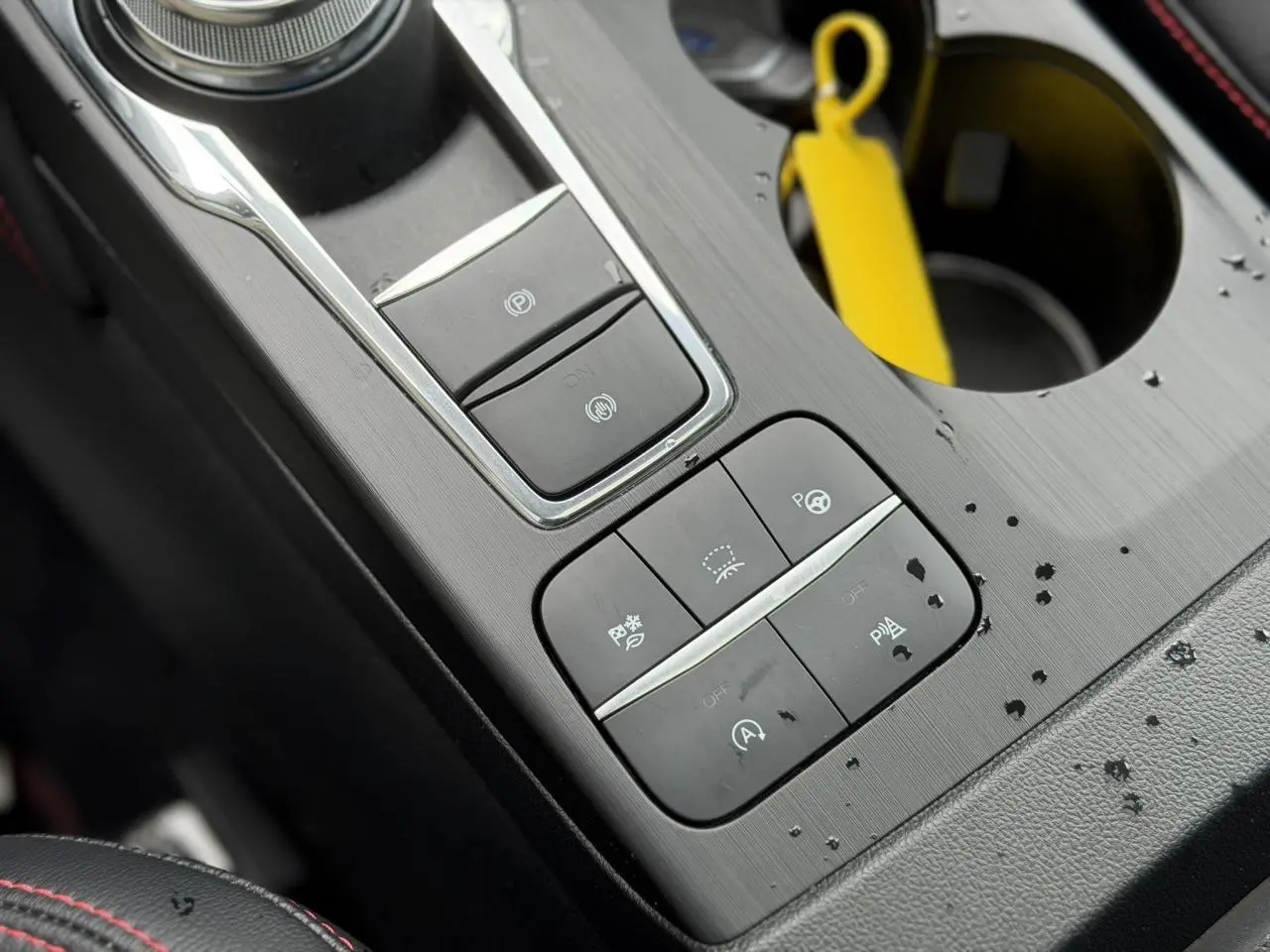 Gros plan sur la console centrale noire avec commandes électroniques et porte-gobelet du Ford Kuga 2023 noir Agathe.