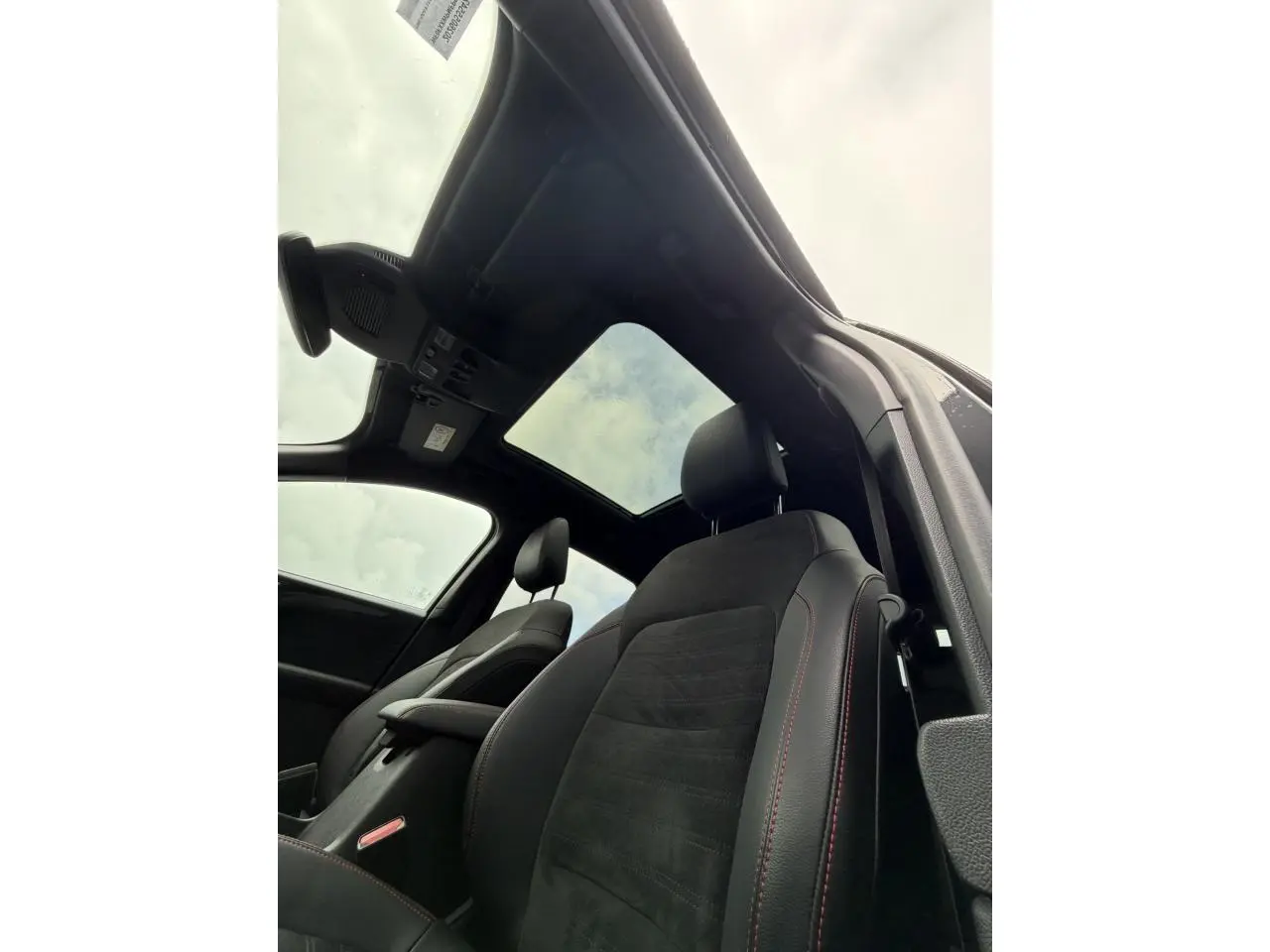 Vue intérieure du Ford Kuga 2023 noir Agathe, sièges avant avec surpiqûres rouges et toit ouvrant panoramique.