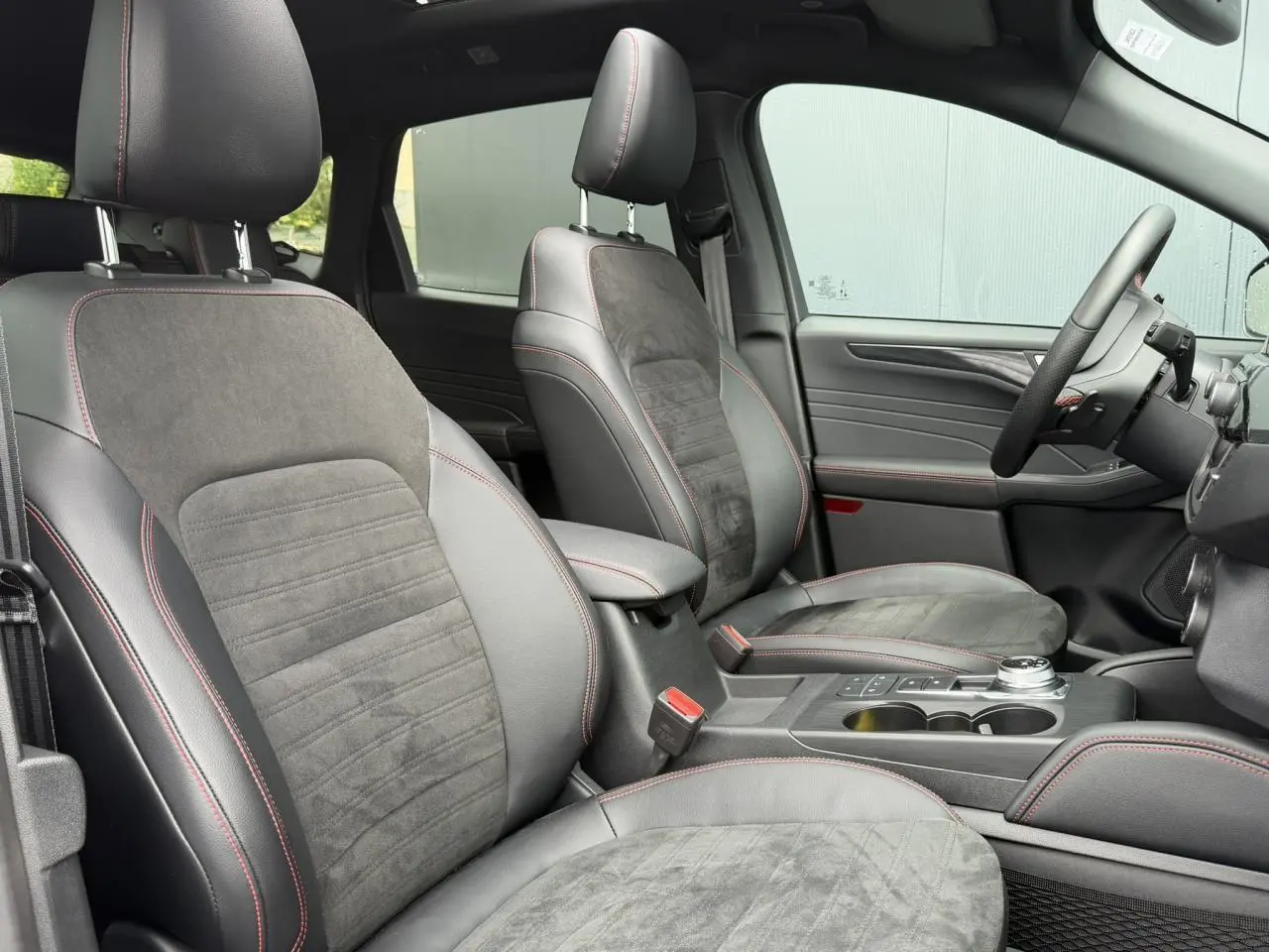 Vue intérieure côté conducteur du Ford Kuga 2023, sièges cuir et alcantara noirs avec surpiqûres rouges et console centrale.