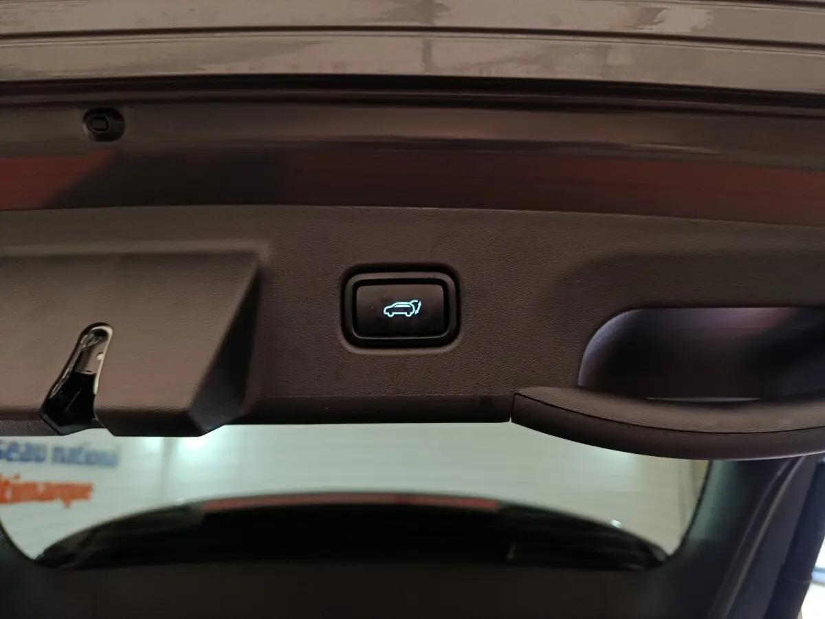 Gros plan sur le bouton d'ouverture électrique du coffre, intérieur du hayon d’un Hyundai Tucson gris foncé 2025.