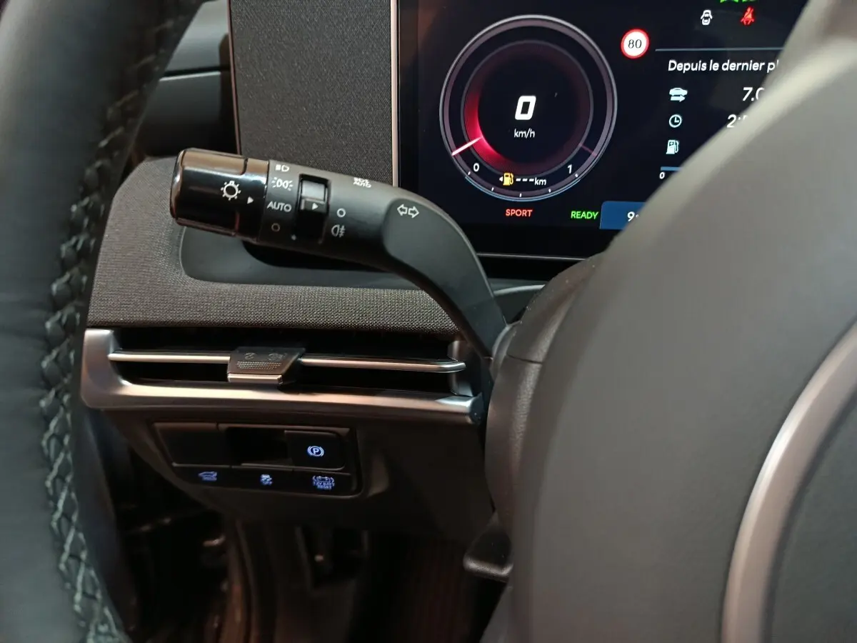 Gros plan sur le combiné d'instruments numérique et la commande des feux à gauche du volant du Hyundai Tucson gris foncé 2025.