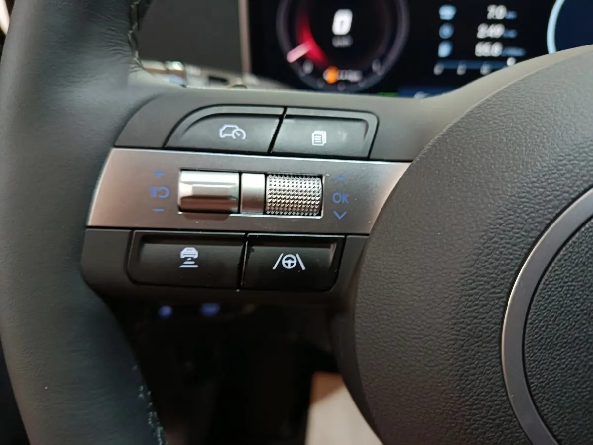 Gros plan sur les commandes multifonctions à gauche du volant cuir du Hyundai Tucson gris foncé 2025 hybride.
