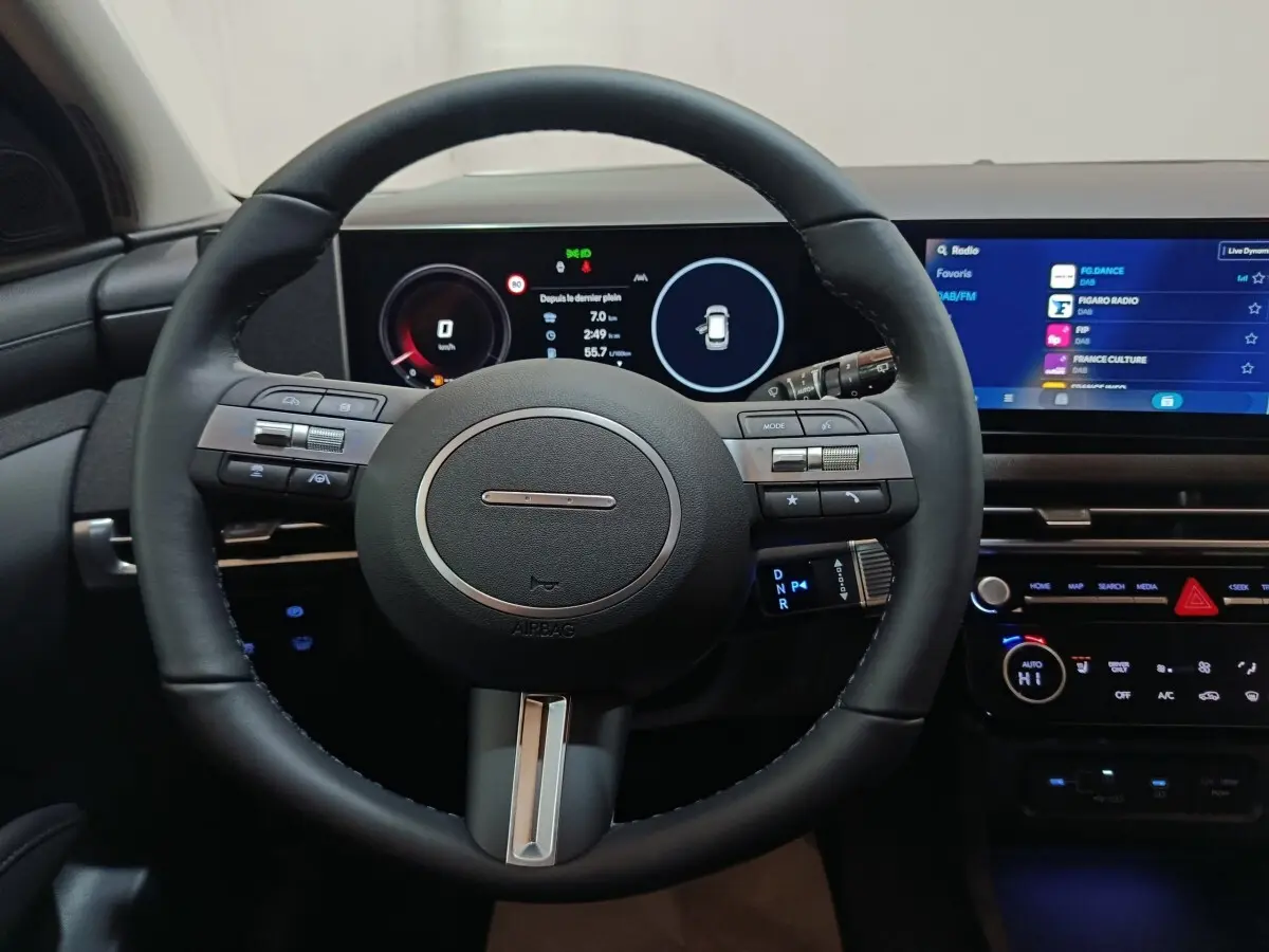 Vue intérieure centrée sur le volant cuir noir et le tableau de bord numérique du Hyundai Tucson 2025 hybride.