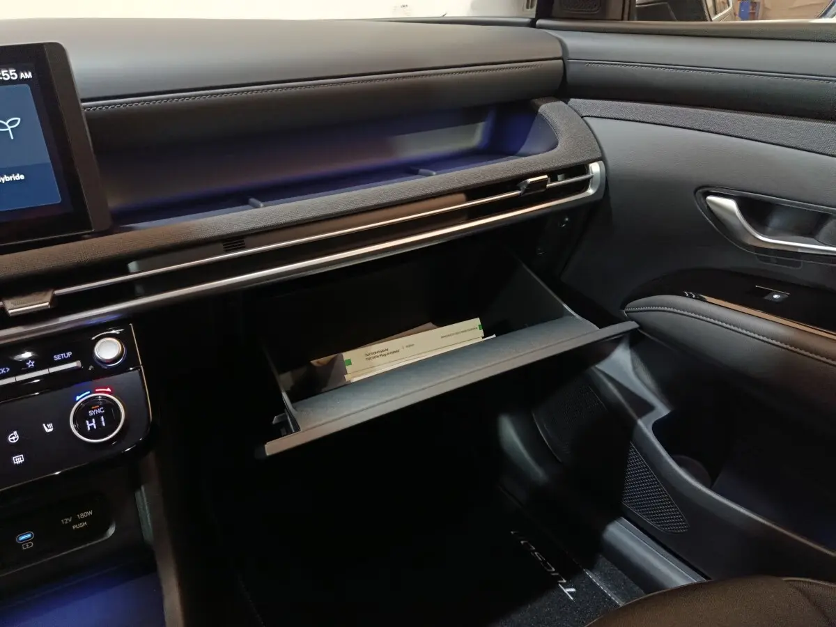 Intérieur du Hyundai Tucson 2025 gris foncé, vue côté passager avec boîte à gants ouverte et tableau de bord moderne.