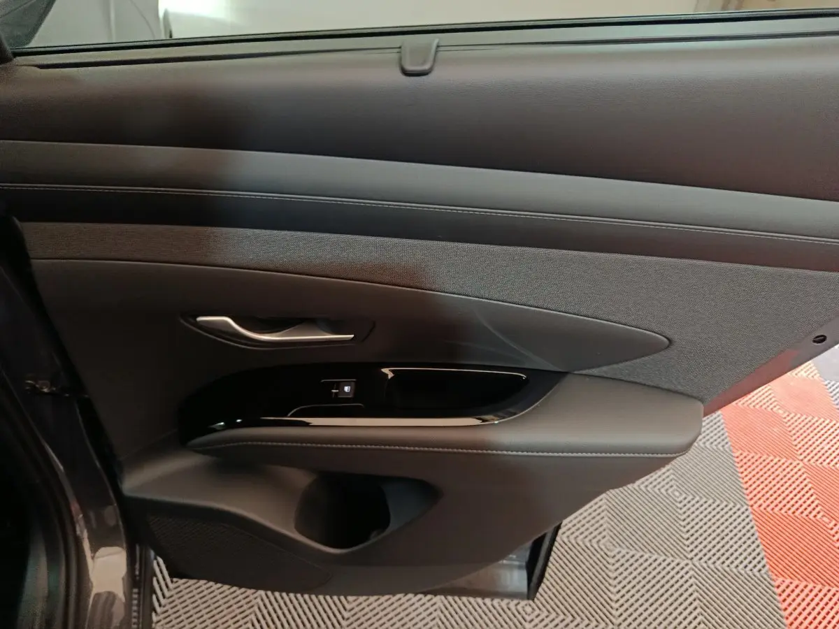 Vue intérieure du panneau de porte avant gauche du Hyundai Tucson 2025 gris foncé, avec commandes électriques et finition tissu et cuir.