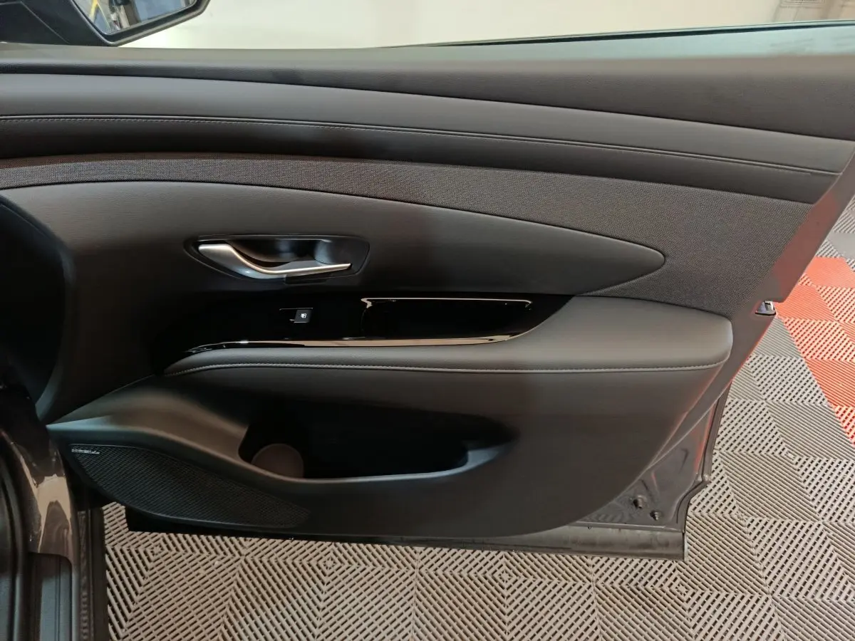 Vue intérieure de la porte avant gauche grise du Hyundai Tucson 1.6 Hybrid 239 Creative avec garniture noire et poignée chrome.