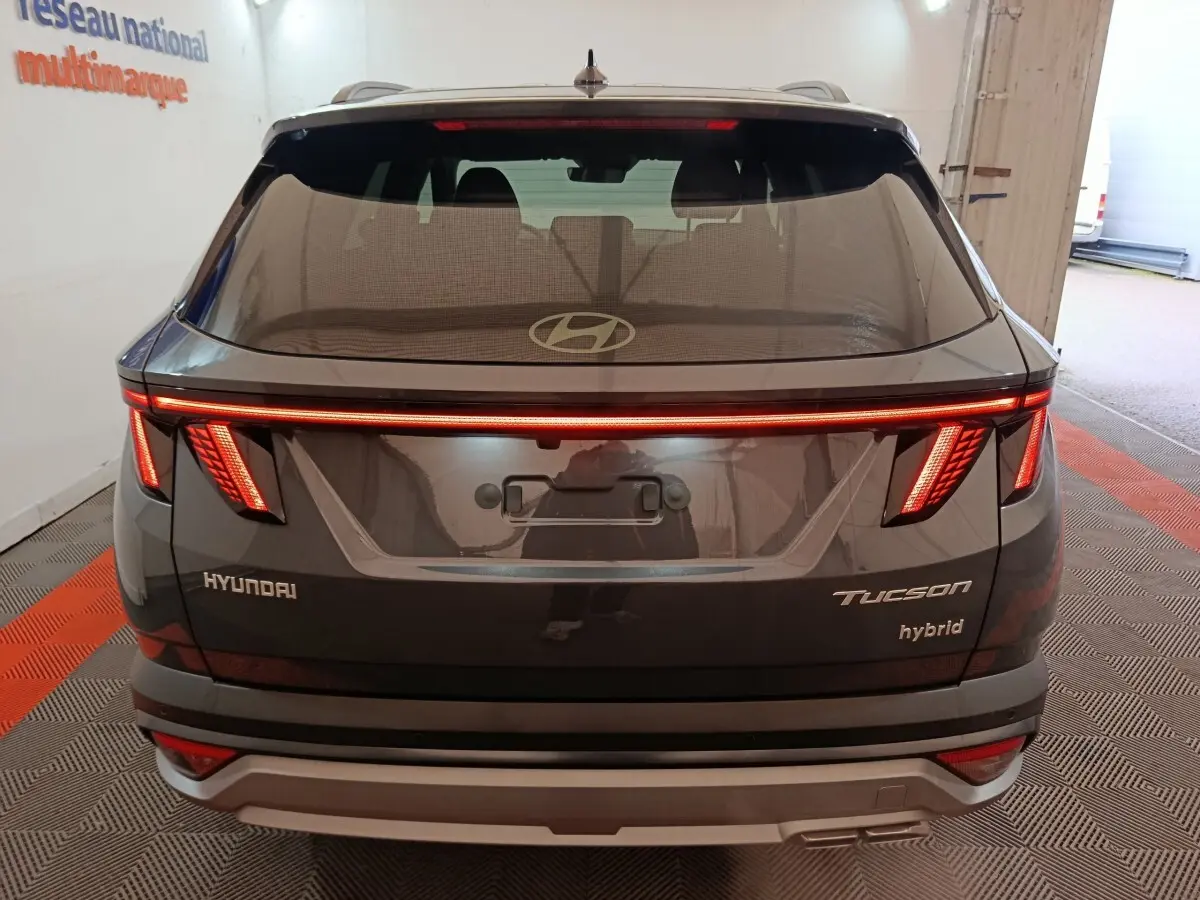 Vue arrière d’un Hyundai Tucson hybride gris foncé avec feux LED allumés et logo Hyundai visible sur le hayon.