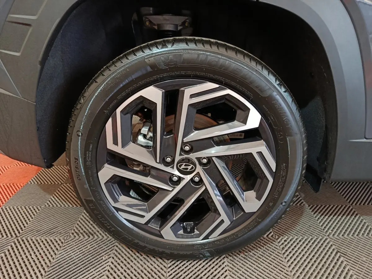 Gros plan sur la jante avant droite du Hyundai Tucson gris foncé, avec design géométrique bicolore et logo Hyundai central.