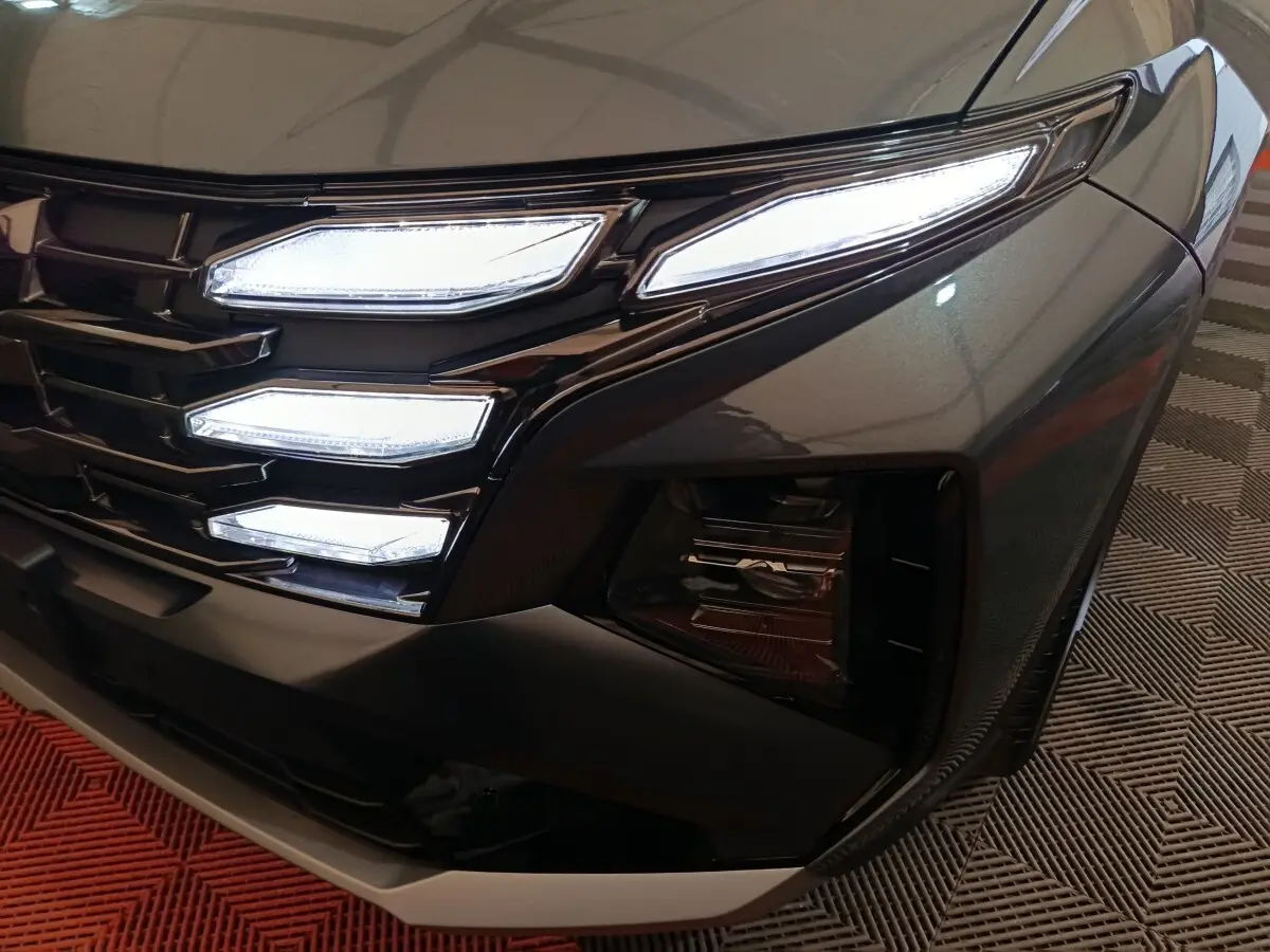 Gros plan sur le phare avant droit et la calandre noire du Hyundai Tucson 2025 gris foncé avec éclairage LED distinctif.