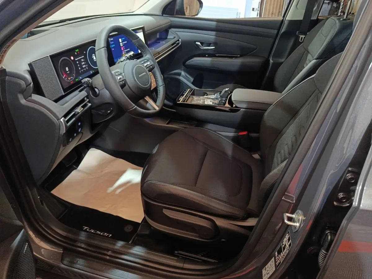 Intérieur avant droit du Hyundai Tucson gris foncé 2025, avec tableau de bord numérique et sièges noirs.