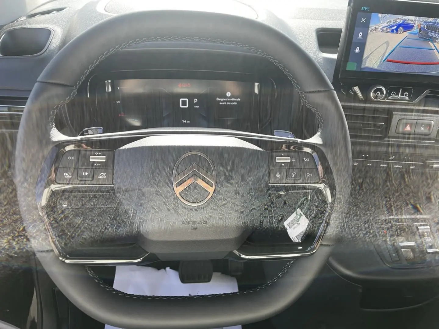 Vue intérieure centrée sur le volant noir du Citroën Berlingo 2026 avec tableau de bord digital et écran de caméra de recul.