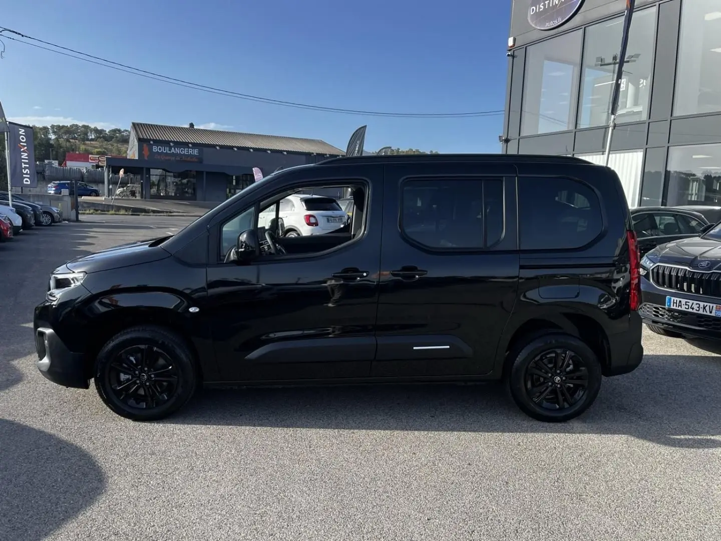 Profil côté gauche d'un Citroën Berlingo noir Perla Nera avec jantes noires, stationné en extérieur au soleil.