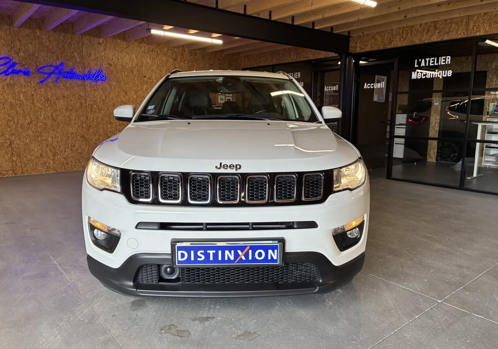 Jeep Compass ivoire vue de face en intérieur, avec calandre noire et plaques Distinxion visibles.
