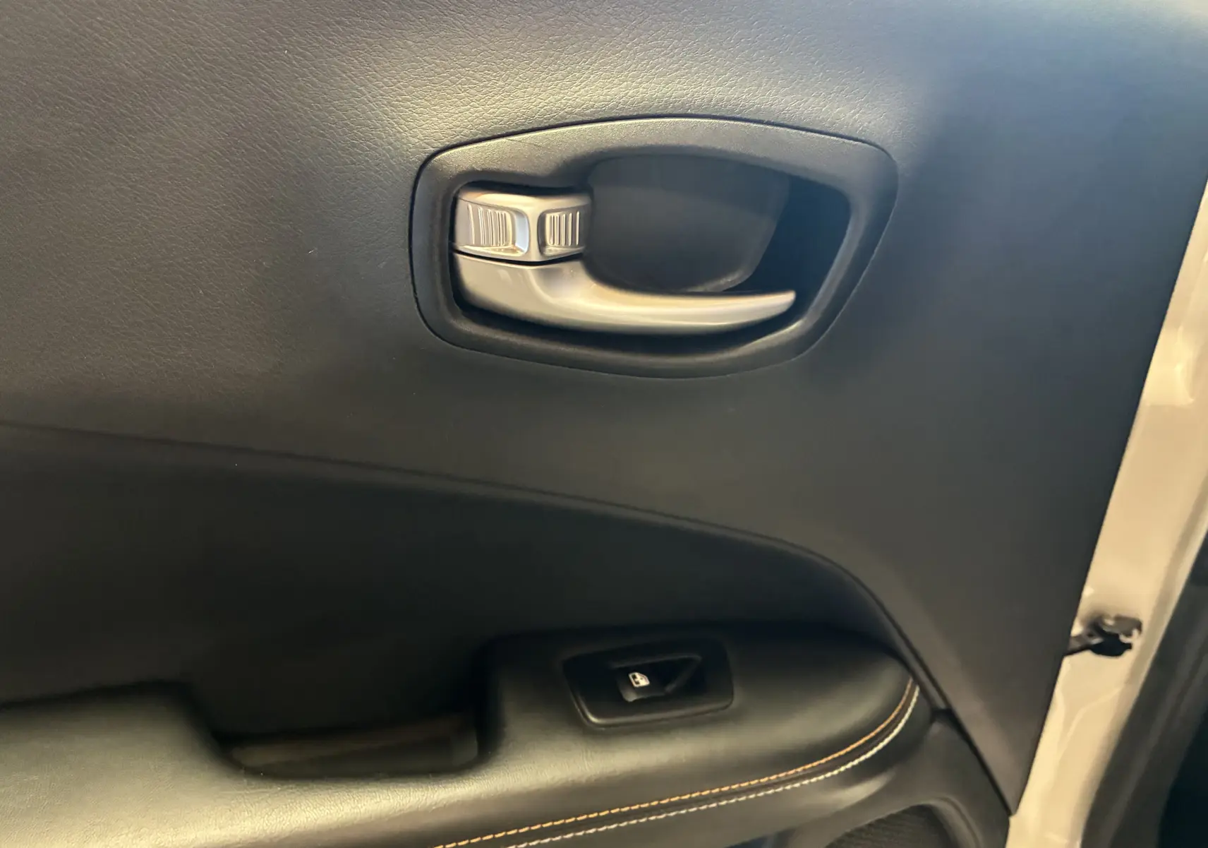 Gros plan sur la poignée intérieure et le bouton de verrouillage de la porte côté gauche du Jeep Compass ivoire.