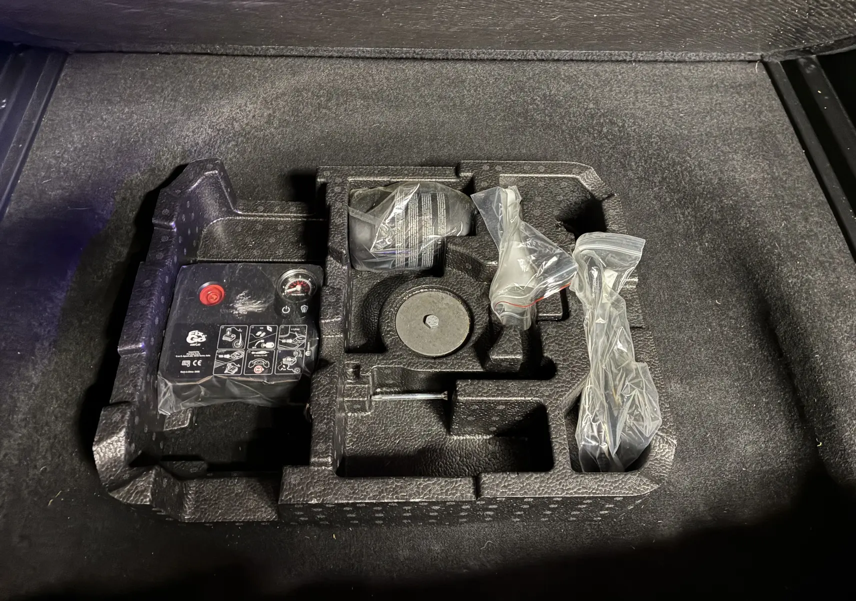 Gros plan sur le rangement sous coffre du Jeep Compass ivoire, montrant le kit de réparation pneu et outils emballés.